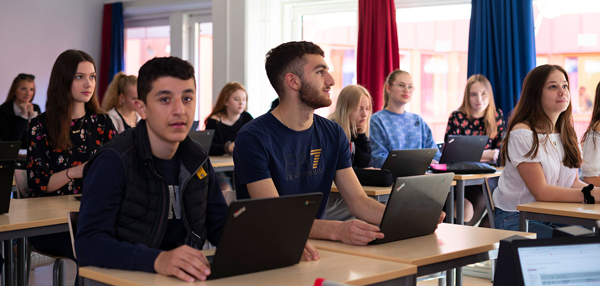Gymnasieelever med bärbara datorer uppslagna i klassrum 