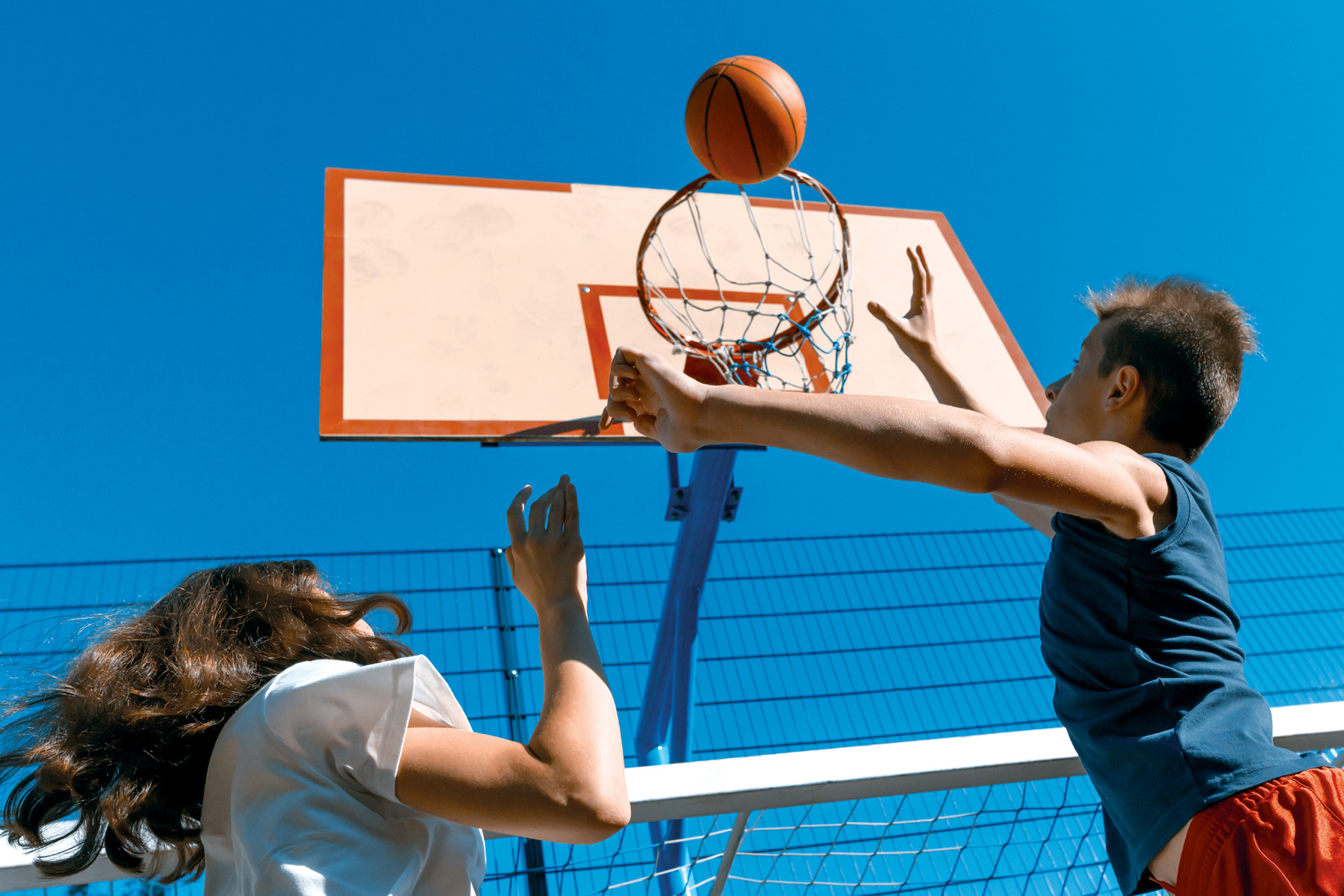 Två barn som spelar basket i solen.