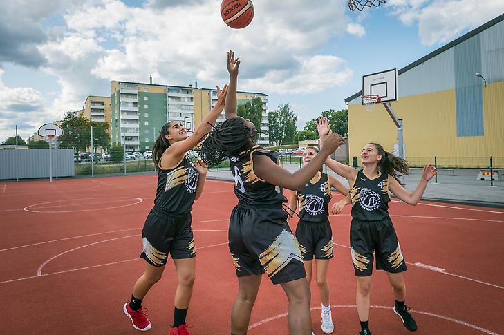 Unga kvinnor spelar basket på en utomhusplan.
