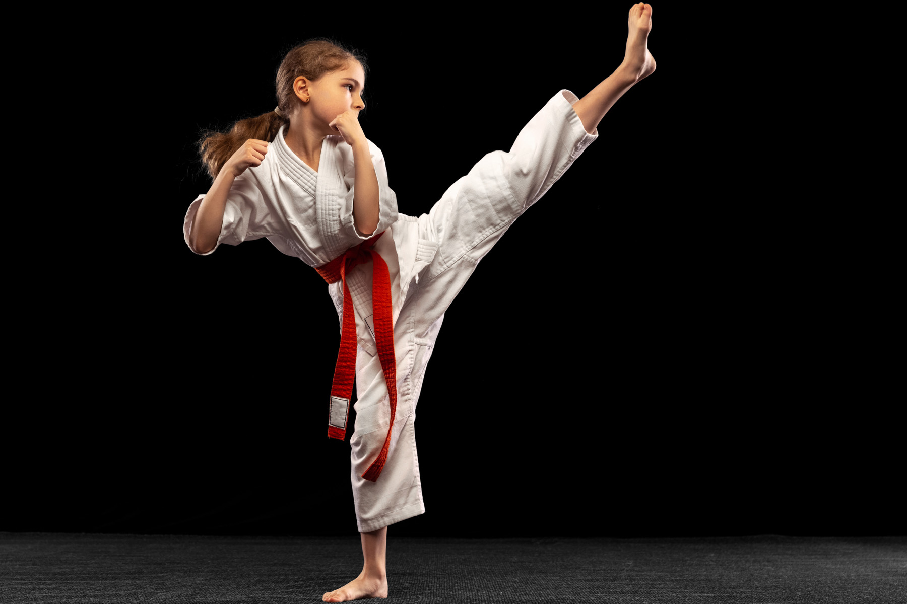 En flicka i judodräkt som sparkar i luften.