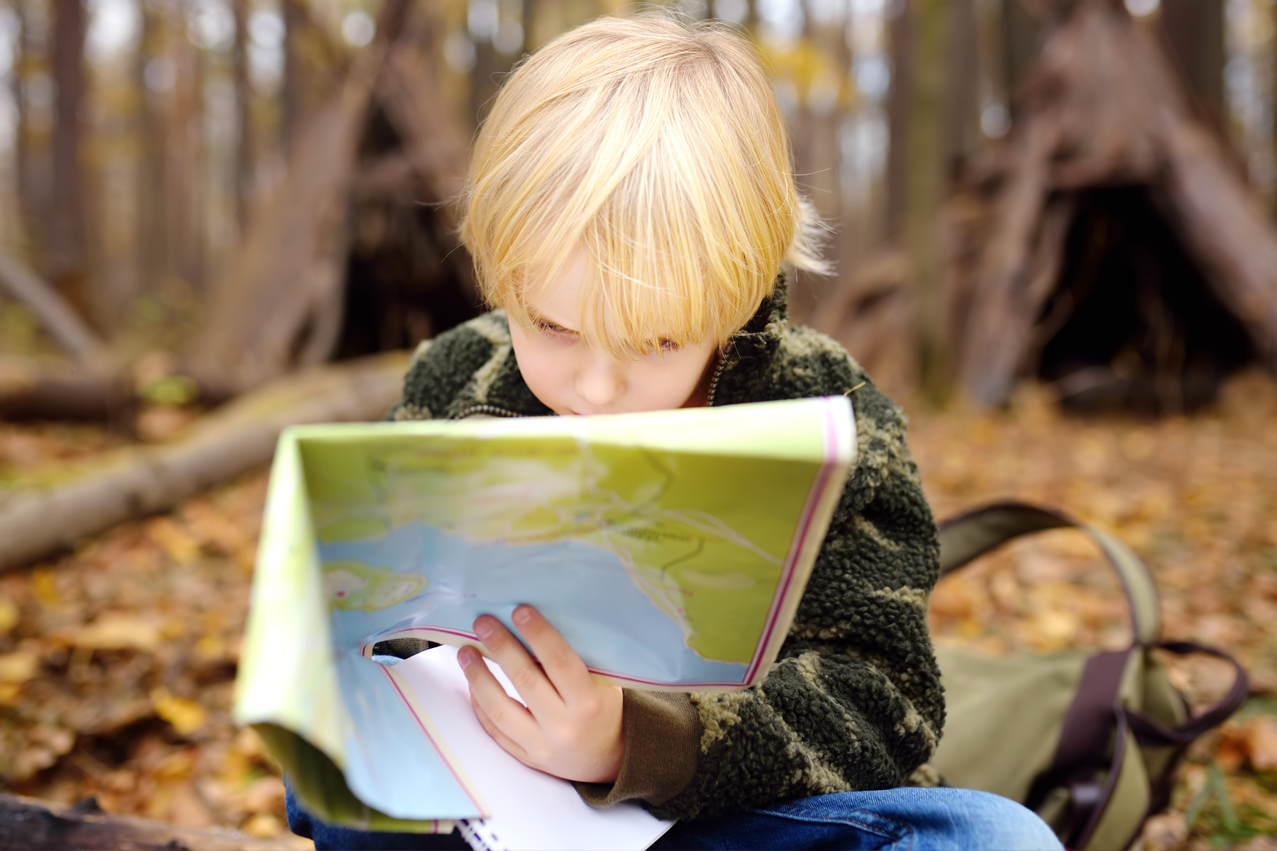 Ett barn sitter i skogen och studerar en karta.