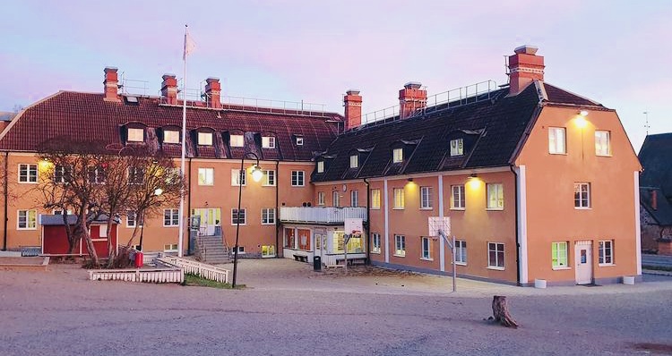 Skolbyggnad på Botkyrka Friskola. Skymmning, lampor som lyser upp den skära byggnaden.