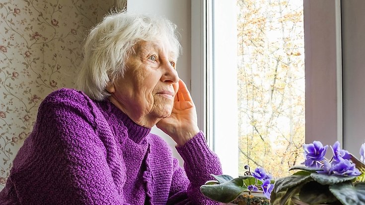 En äldre kvinna sitter och tittar ut genom sitt fönster.